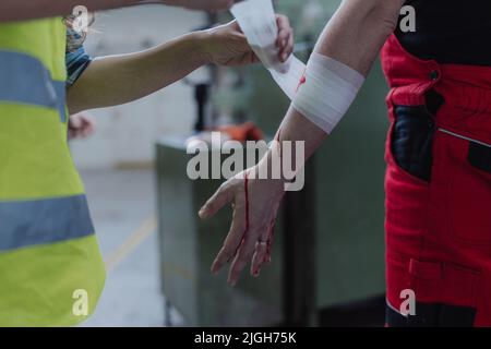 Woman is helping her colleague after accident in factory. First aid support on workplace concept. Stock Photo