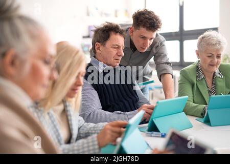 Group of seniors attending IT class in community centre with teacher Stock Photo