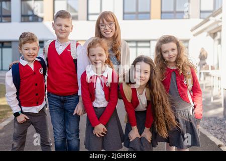 Portrait of happy schoolkids in uniforms with teacher at schoolyard, looking at camera. Stock Photo
