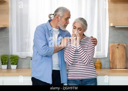 Caring Senior Man Comforting His Crying Wife In Kitchen At Home Stock Photo