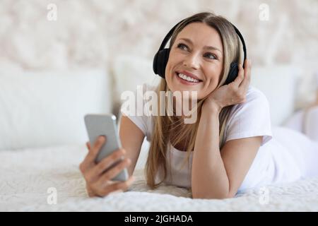 Dreamy young lady using smartphone and headset at home Stock Photo