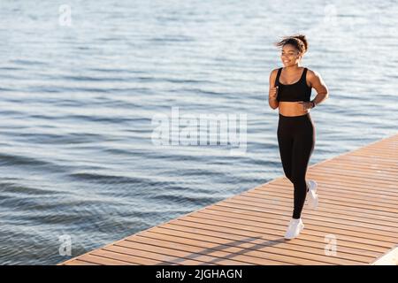 Happy black lady jogging by city lake in the park Stock Photo