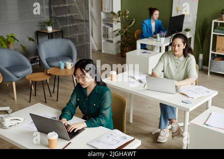 High angle view of female operators in headphones sitting at their workplaces with computers and cooperating with customers at call centre Stock Photo