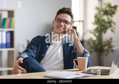 Break At Work. Smiling Young Male Entrepreneur Talking On Cellphone At Workplace Stock Photo