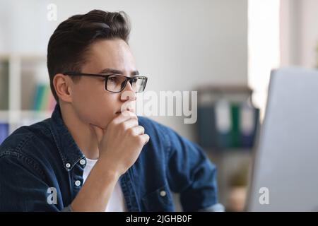 Portrait Of Pensive Young Male Entrepreneur In Eyeglasses Sitting At Workplace Stock Photo