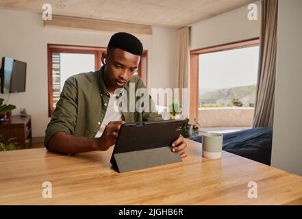 Young adult African American male using pen to write on electronic tablet. Sitting focussed, working remotely from modern home. Stock Photo