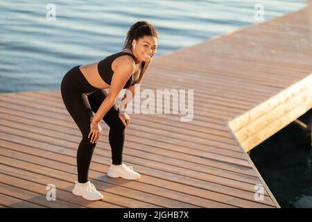 Happy black lady jogging by seaside, having break Stock Photo