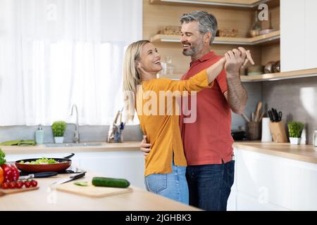 Romantic middle aged couple dancing while cooking together Stock Photo