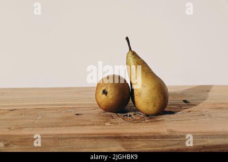 Autumn, summer fruit still life. Two yellow pears on old rustic wooden table backgound in sunset light. Blurred beige wall, soft long shadows Stock Photo