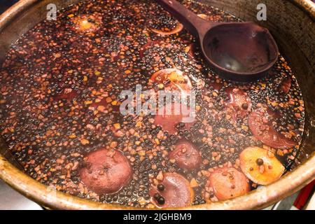 Bowl of traditional hot spicy mulled wine with cinnamon sticks, cloves, oranges and apples on sale at Bath Christmas market. Stock Photo