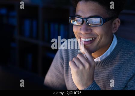 Close-up of smiling asian male professional wearing eyeglasses with finger on chin using computer Stock Photo