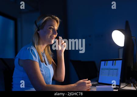 Female caucasian customer service executive talking over headset and using computer at desk Stock Photo