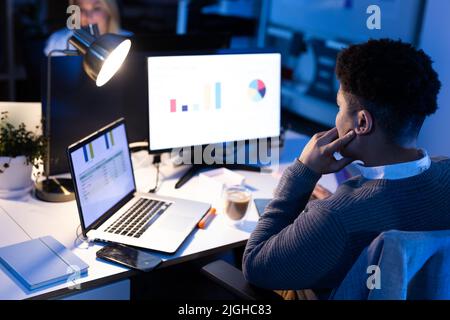 Asian male professional analyzing charts and spreadsheet over computer and laptop on desk in office Stock Photo