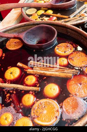 Bowl of traditional hot spicy mulled wine with cinnamon sticks, cloves, oranges and apples on sale at Bath Christmas market. Stock Photo