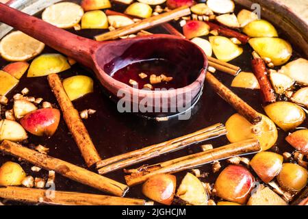 Bowl of traditional hot spicy mulled wine with cinnamon sticks, cloves, oranges and apples on sale at Bath Christmas market. Stock Photo