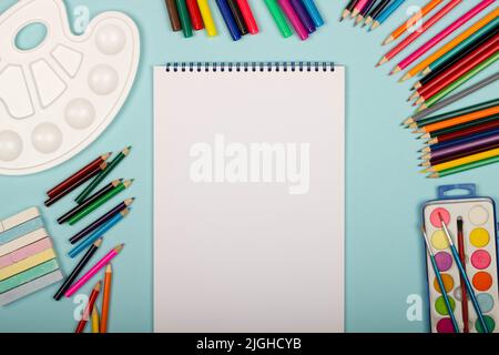 Art supplies for school painting and a blank sheet of paper on a vertical sketchbook on a blue background with copy space for text. Colorful pencils, Stock Photo