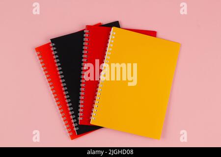 Multicolored notebooks, black, red and orange, on a pink background with copy space for text. Top view. Back to school Stock Photo