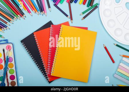 Multicolored notebooks, black, red and orange, art school supplies for painting, on a blue background with copy space for text. Colorful pencils, mark Stock Photo