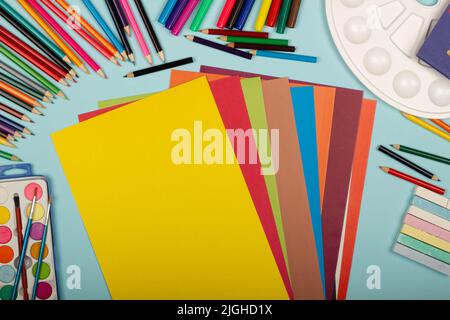 Art school supplies for painting and a set of colored paper on a blue background with copy space for text. Colorful pencils, markers, paints, crayons. Stock Photo