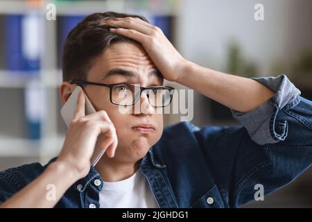Pff. Stressed Young Man Talking On Mobile Phone And And Touching Head Stock Photo