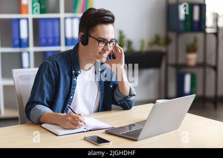 Young Male Office Employee Wearing Headset Watching Online Webinar At Workplace Stock Photo