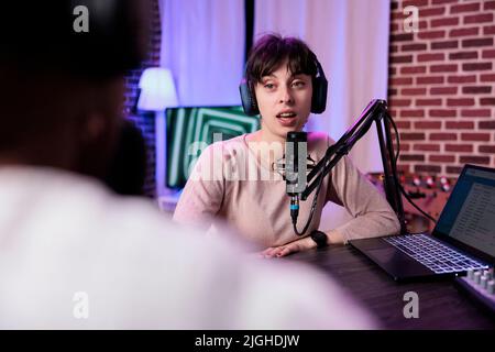 Lifestyle blogger having conversation with female guest, recording podcast with sound equipment. Influencer talking to cheerful woman to broadcast live discussion to record in studio. Stock Photo