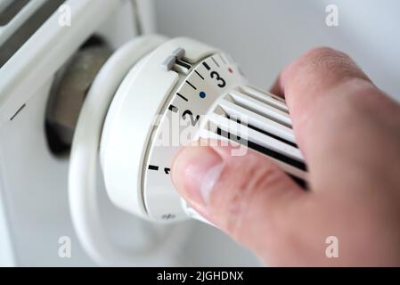 person adjusting thermostat on radiator to lower temperature, saving energy and money concept Stock Photo