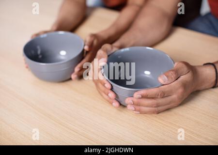 Hands of hungry young african american wife and husband holding empty plates on table in kitchen Stock Photo