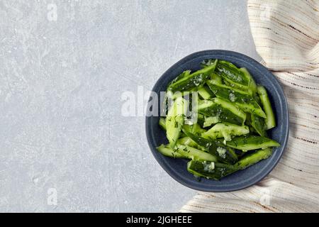Smashed lightly salted broken cucumbers in a ceramic bowl and kitchen towel napkin. Top view with copy space Stock Photo