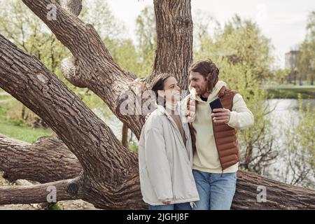 Young happy couple enjoying each other during their walking in the park, they making selfie against big tree Stock Photo
