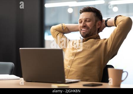 Man Using Laptop Holding Hands Behind Head Resting In Office Stock Photo