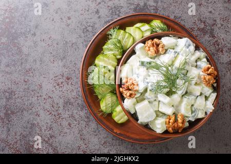Summer salad of cucumbers, garlic, dill and walnuts seasoned with yogurt close-up in a bowl on the table. Horizontal top view from above Stock Photo