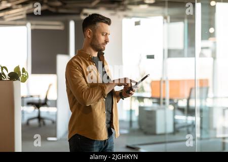 Male Entrepreneur Using Digital Tablet Working Standing In Modern Office Stock Photo