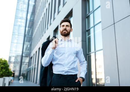 Confident handsome european millennial bearded businessman with jacket on shoulder Stock Photo