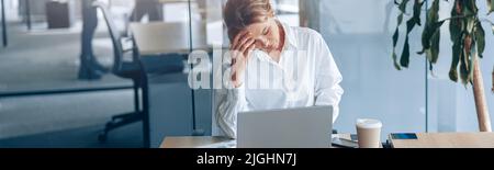 Tired businesswoman with headache working on laptop at her workplace at modern office Stock Photo