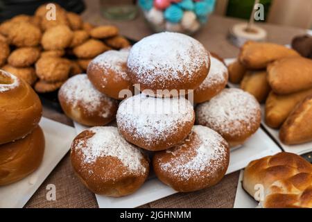 several buns lying on the table in a slide covered with powdered sugar. sweet pies with powdered sugar on the table or counter in the store. Stock Photo