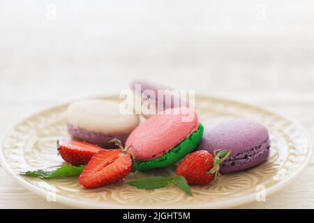 Sweet colorful macaroons with strawberry slices on plate copyspace. Front view on white glass plate with colorful macaroons served with fresh strawber Stock Photo