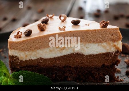 Front view on layered chocolate souffle cake close-up. Peace of cocoa biscuit on black plate, decorated with mint leaves and coffee beans Stock Photo