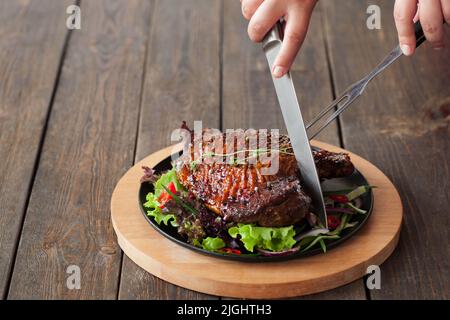 Grilled duck thigh cutting with cutlery on wooden background, eating at restaurant concept, front view Stock Photo