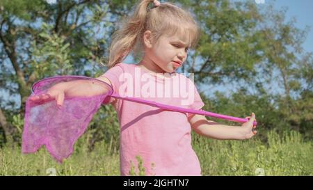 Odessa, Ukraine, Eastern Europe. 10th July, 2022. Little girl plays with butterfly net of tall grass in city park. Cute little girl is playing with aerial insect net in meadow on sun day. (Credit Image: © Andrey Nekrasov/ZUMA Press Wire) Stock Photo