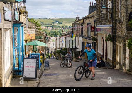 Haworth, West Yorkshire, UK. Two cyclists pushing their bikes up the steep, Main Street hill in Haworth. Stock Photo