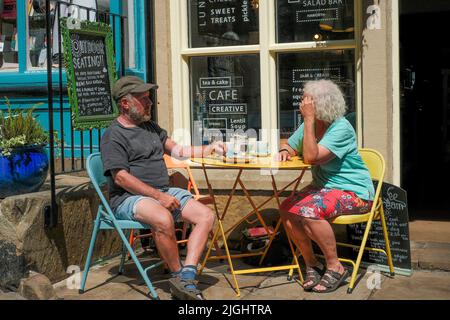 Haworth, West Yorkshire, UK. An elderly couple relaxing outside in the sunshine at a cafe on Main Street Haworth. Stock Photo