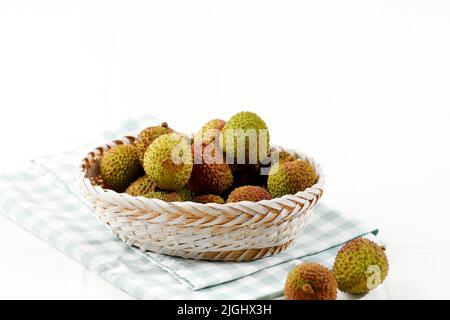 Green Lychee Fruit on Rattan Basket, Isolated on White Table. with Checkered Napkin. Copy Space for Text Stock Photo