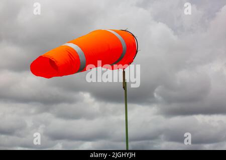 Windsock indicator of wind on tank chemical cone indicating wind direction and force. Horizontally flying windsock (wind vane) with cloud sky in the b Stock Photo