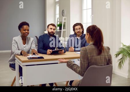 Friendly group of HR employees during interview in office talk to woman with job applicant. Stock Photo