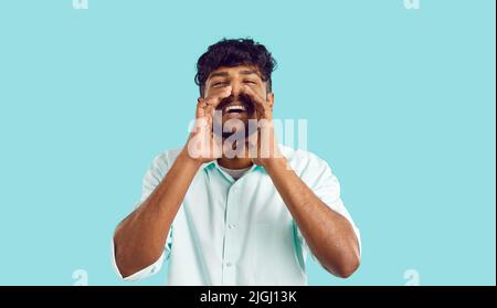 Studio portrait of happy young Indian man holding his hands at his mouth and shouting Stock Photo