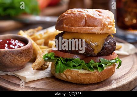 Cheeseburger with lettuce and tomato on toasted bun with french fries and ketchup on wooden platter Stock Photo