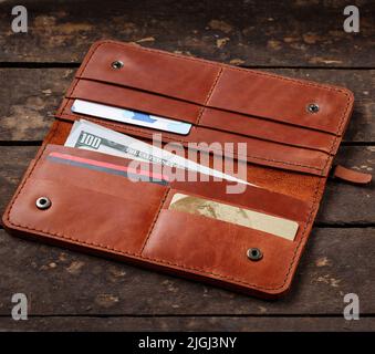 Leather red wallet with money and credit cards on old wooden background. Business and wealth concept. Stock Photo