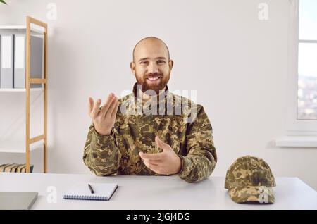 Happy soldier sitting at office desk, having conference call, speaking and smiling Stock Photo