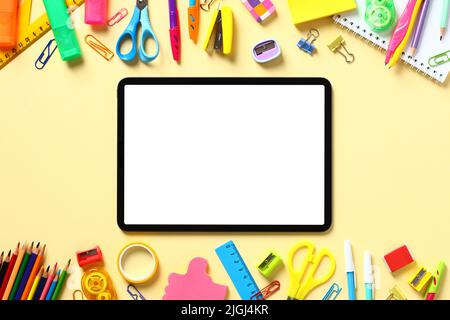 Digital tablet with blank white screen and frame of colorful school supplies on yellow background. Online school, distance e-learning concept. Flat la Stock Photo